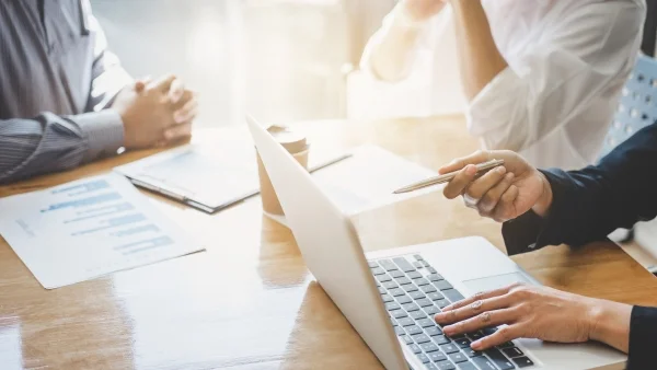 Geschäftsleute analysieren Dokumente und Laptop am Tisch, datenbasierte Entscheidungsfindung und professionelle Zusammenarbeit im Consulting.