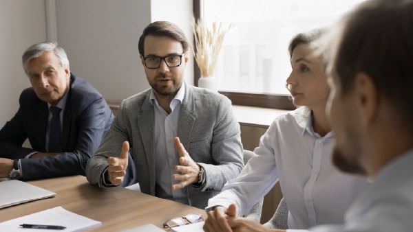Teammeeting im Büro: Manager erklärt engagiert Strategie, Kollegen hören aufmerksam zu, Leadership und Zusammenarbeit im Mittelpunkt.