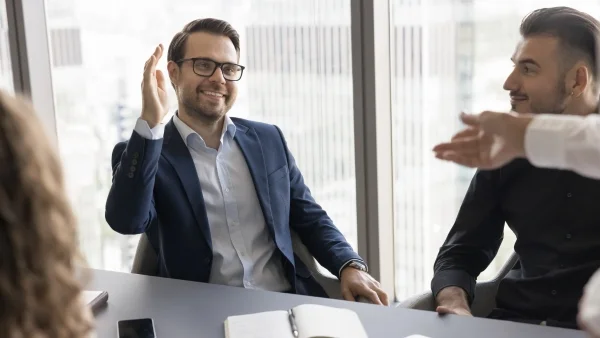 Teilnehmer diskutieren im Meeting, Trainer motiviert mit Handzeichen, aktiver Austausch und Praxisbezug bei Sales Trainings.