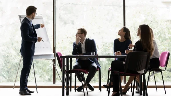 Teilnehmer diskutieren im Meeting, Trainer motiviert mit Handzeichen, aktiver Austausch und Praxisbezug bei Sales Trainings.