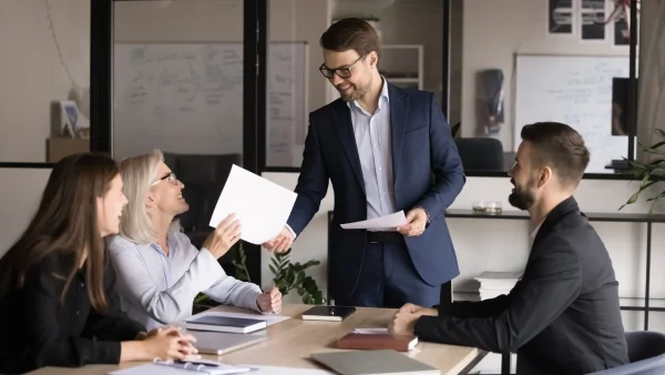 Trainer überreicht Unterlagen im Meeting, Teilnehmer diskutieren aktiv und fördern Zusammenarbeit durch Seminare Persönlichkeitsentwicklung im Büro.