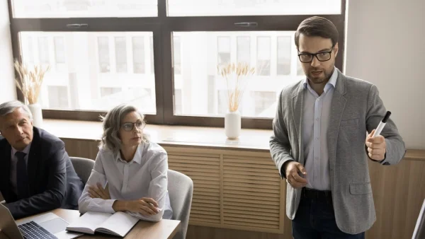 Berater präsentiert im Meeting vor Kollegen am Tisch, strategische Analyse und Beratungssituation bei Lessig Consulting.