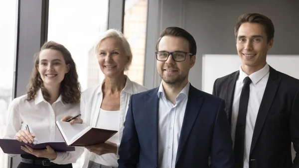 Vier Geschäftsleute stehen lächelnd im Büro, symbolisieren Teamwork, Vertrauen und Erfolg durch professionelle Beratung bei Lessig Consulting.