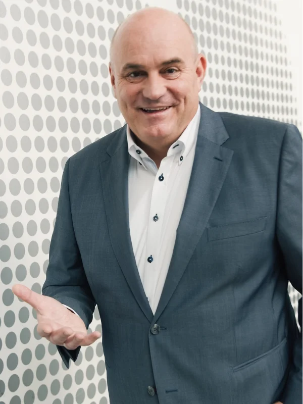 Lächelnder Geschäftsmann im grauen Anzug vor gepunkteter Wand, professionelles Porträt für Lessig Consulting.